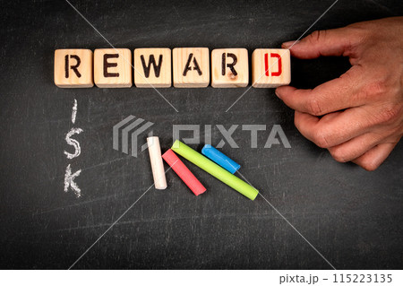 REWARD and RISK. Wooden block crossword puzzle and pieces of chalk on a chalkboard background REWARD and RISK. Wooden block crossword puzzle and pieces of chalk on a chalkboard background 115223135