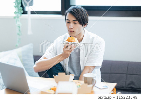 パソコンを見ながらデリバリーで注文した料理を食べる男性 パソコンを見ながらデリバリーで注文した料理を食べる男性 115223349