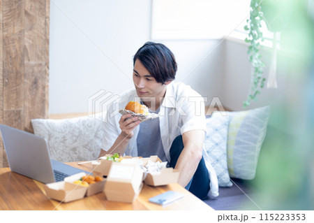 パソコンを見ながらデリバリーで注文した料理を食べる男性 パソコンを見ながらデリバリーで注文した料理を食べる男性 115223353