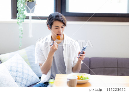 スマホを見ながら食事をする男性 115223622