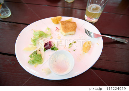 Leftover food on a white plate on wooden table, close-up. Food and drink consumerism. View from above 115224929
