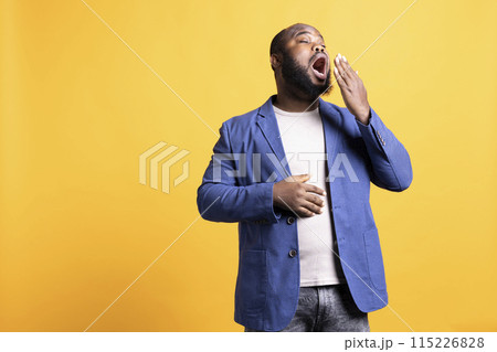 African american man feeling exhausted and yawning, covering his mouth, isolated over studio background. BIPOC person being sleepy during morning, awaken too early, showing sleepiness African american man feeling exhausted and yawning, covering his mouth, isolated over studio background. BIPOC person being sleepy during morning, awaken too early, showing sleepiness 115226828