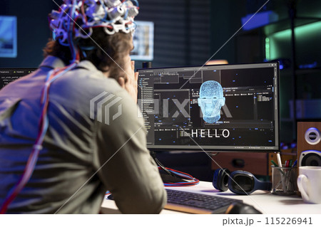 IT professional using EEG headset to communicate with artificial intelligence on computer in binary code. Software developer sending brainwave signals to AI entity on PC using high tech device IT professional using EEG headset to communicate with artificial intelligence on computer in binary code. Software developer sending brainwave signals to AI entity on PC using high tech device 115226941