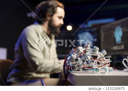 Focus on EEG headset used by engineer in blurry background to upload consciousness into computer. Close up shot of high tech gear used by IT expert to create connection between brain and PC 115226975