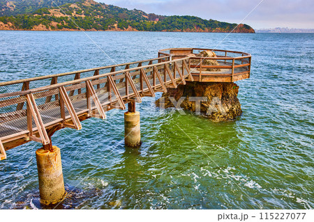 Choppy water around Elephant Rock pier with clear coastline and distant city across bay 115227077