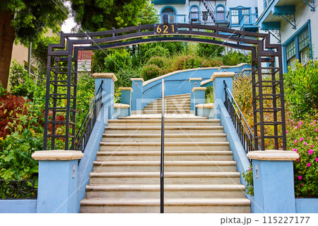Center of staircase with metal fame going uphill to large blue house with large flowering garden 115227177
