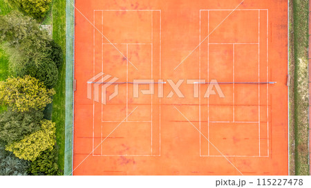 This aerial view captures two clay tennis courts surrounded by vibrant greenery and trees 115227478