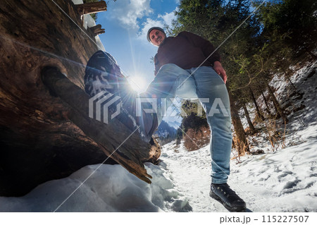 Funny tourist stands with one foot on a fallen tree while traveling along a hiking winter mountain trail. Funny tourist stands with one foot on a fallen tree while traveling along a hiking winter mountain trail. 115227507