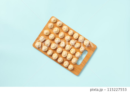 Top view of a wooden board with neatly laid out semi-cooked dumplings on blue background. 115227553