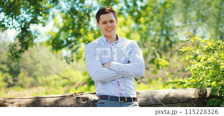 Handsome happy smiling teenager boy, young guy with crossed arms in shirt standing outdoors 115228326