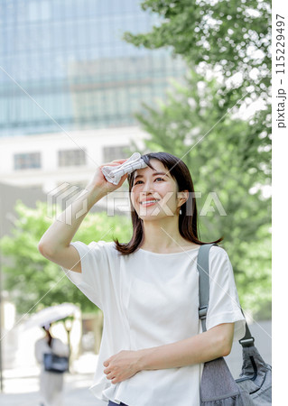 額の汗をハンカチで拭き陽射しを気にする女性 額の汗をハンカチで拭き陽射しを気にする女性 115229497