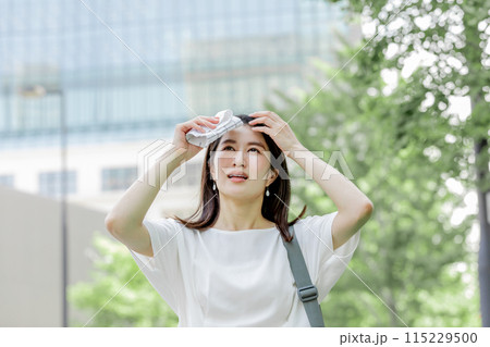 額の汗をハンカチで拭き陽射しを気にする女性 115229500