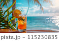 cold cocktail in glass with straw and ice on the table on the beach, ocean and palm leaf as background 115230835