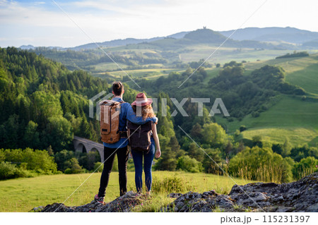 Travellers couple hiking on easy trail in nature with backpacks. Young tourist resting, enjoying breathtaking view. Summer vacation oudoors. Rear view. Travellers couple hiking on easy trail in nature with backpacks. Young tourist resting, enjoying breathtaking view. Summer vacation oudoors. Rear view. 115231397