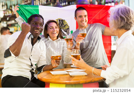 Friends gathered together to watch soccer football championship and celebrating with glasses of beer. Girl holding flag of Mexico 115232054