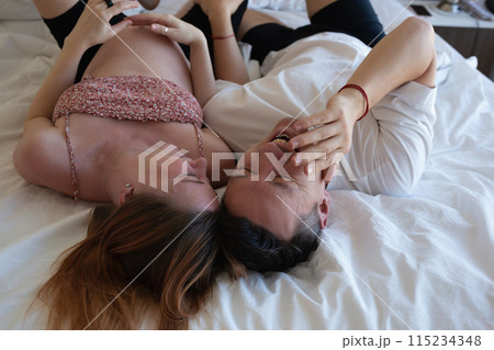 A joyful couple laughing in bed, sharing a playful and intimate moment together A joyful couple laughing in bed, sharing a playful and intimate moment together 115234348