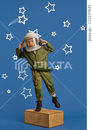 Portrait of young dreamer, little boy in pilot's uniform and helmet aiming high among stars against blue background. Portrait of young dreamer, little boy in pilot's uniform and helmet aiming high among stars against blue background. 115237645