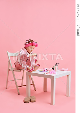 Little spa lover. beautiful little girl, in pajama doing beauty procedures, manicure against pastel pink studio background. 115237758