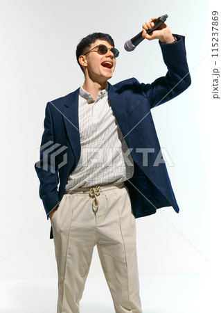 Man dressed casual attire with sunglasses performing, singing with microphone against white studio background. 115237869