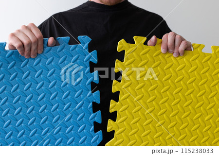 Man holding 2 parts of puzzles blue and yellow color. Idea of Ukrainian flag. 115238033