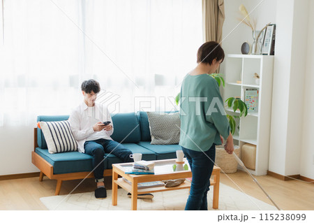 掃除をする女性とスマホをいじる男性 掃除をする女性とスマホをいじる男性 115238099