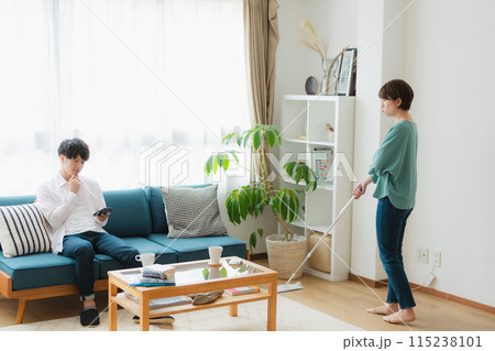 掃除をする女性とスマホをいじる男性 115238101
