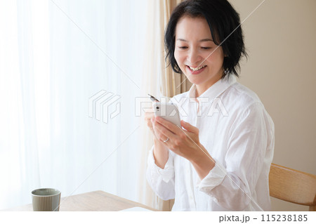 リビングでスマホで情報検索してメモを取るミドル女性 115238185