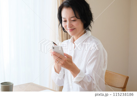 リビングでスマホで情報検索してメモを取るミドル女性 リビングでスマホで情報検索してメモを取るミドル女性 115238186