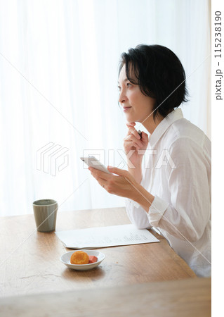 リビングでスマホで情報検索してメモを取るミドル女性 リビングでスマホで情報検索してメモを取るミドル女性 115238190