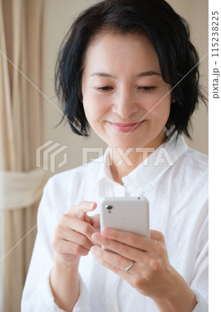 リビングでスマホで情報検索してメモを取るミドル女性 リビングでスマホで情報検索してメモを取るミドル女性 115238225