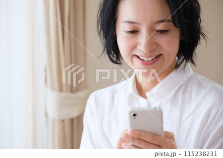 リビングでスマホで情報検索してメモを取るミドル女性 115238231