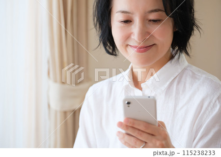 リビングでスマホで情報検索してメモを取るミドル女性 リビングでスマホで情報検索してメモを取るミドル女性 115238233