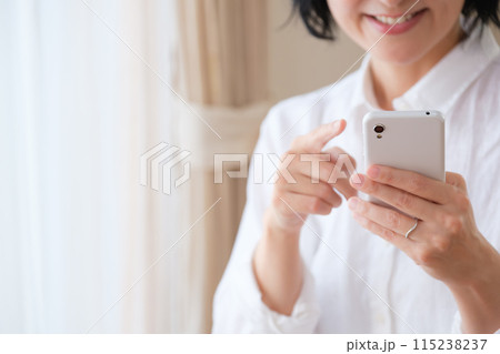 リビングでスマホで情報検索してメモを取るミドル女性 115238237