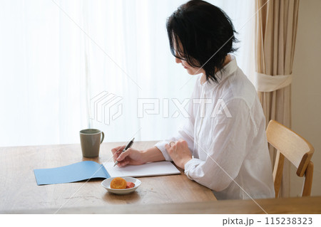 リビングで家族へ手紙を書いているミドル女性 リビングで家族へ手紙を書いているミドル女性 115238323