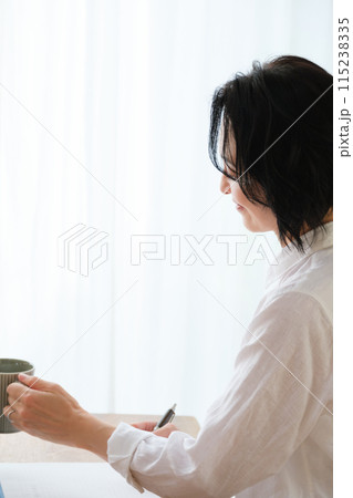 リビングで家族へ手紙を書いているミドル女性 リビングで家族へ手紙を書いているミドル女性 115238335