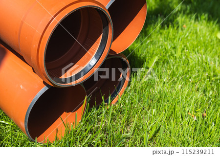 Close up photo of pipes for external sewerage laying on green grass Close up photo of pipes for external sewerage laying on green grass 115239211