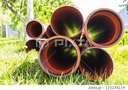 Pipes for external sewerage lay on grass on a sunny day, perspective Pipes for external sewerage lay on grass on a sunny day, perspective 115239214