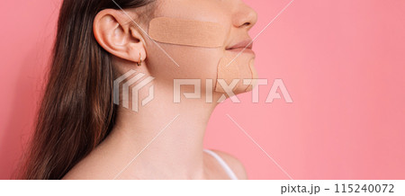 Face tape pasted all over lady's face in profile on pink background Face tape pasted all over lady's face in profile on pink background 115240072