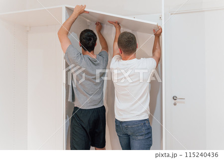 Two carpenters putting up a shelf to assemble a new cabinet. Furniture Concept 115240436