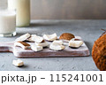 Fresh coconut pieces on a wooden board with a glass and jar of coconut milk in the background, showcasing natural ingredients. 115241001