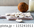 Freshly sliced coconut pieces arranged on a wooden cutting board with a whole coconut and a jar of coconut milk in the background. 115241011