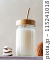 A jar of fresh coconut milk with a bamboo straw, accompanied by stacked coconut slices and a whole coconut on a textured surface. 115241018