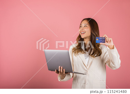 Portrait of Asian beautiful young woman customer showing credit card for online payment shopping transactions cashback loan on laptop studio shot isolated on pink background 115241480