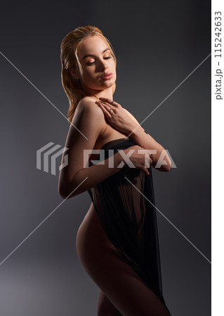 Sensual naked woman covering body with fabric in dark studio 115242633