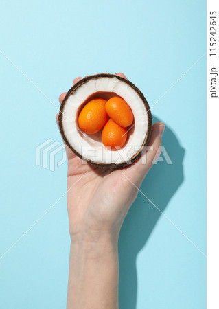 Whole kumquat in half of coconut in hand on blue background, top view 115242645