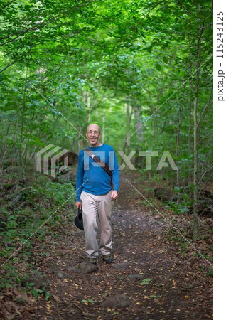 Active senior man hiking on a woodland trail green foliage 115243125