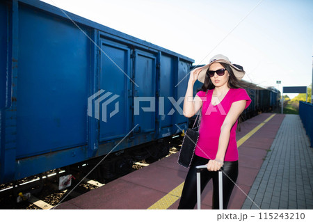 The girl holds her big hat so that the blast from the freight train ahead does not break it. The girl holds her big hat so that the blast from the freight train ahead does not break it. 115243210