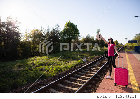 The young woman took off her hat and waves it to make her longed-for train stop. Railway platform in the province. The young woman took off her hat and waves it to make her longed-for train stop. Railway platform in the province. 115243211
