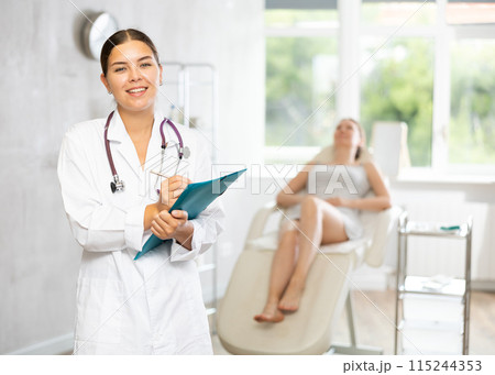 Female doctor of medical clinic stands with folder and fills out documents before manipulations. 115244353