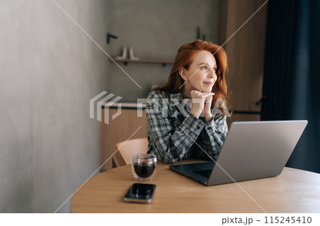Inspired young woman working or studying remotely from home office using laptop, look away, think on good idea with smile. Motivated millennial female enjoy freelance job. Concept of remote work. Inspired young woman working or studying remotely from home office using laptop, look away, think on good idea with smile. Motivated millennial female enjoy freelance job. Concept of remote work. 115245410
